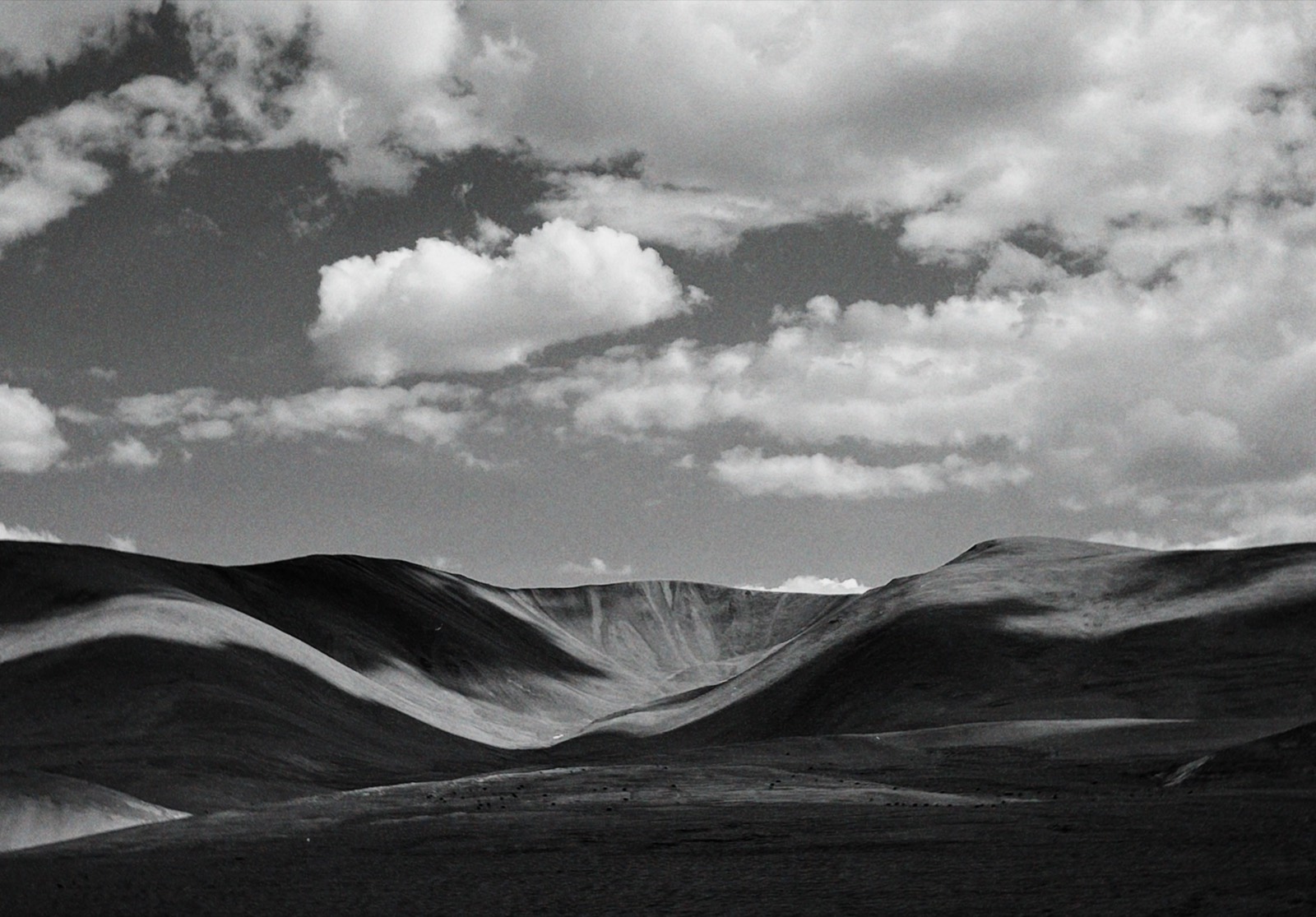 Black-and-white landscape of rolling hills under layered clouds